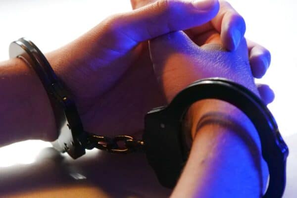 close-up-of-handcuffed-hands-under-blue-police-light-signifying-arrest-or-detention - Adam C. Gynac & Associates LLC Understanding Orders of Protection Granholm and Gynac Joliet Page 4